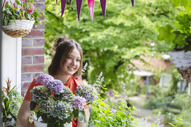 Smiling teenage girl with hydrangea flowers on balcony - IHF01103