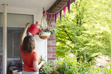 Mädchen bewässert hängenden Blumentopf auf dem Balkon - IHF01104