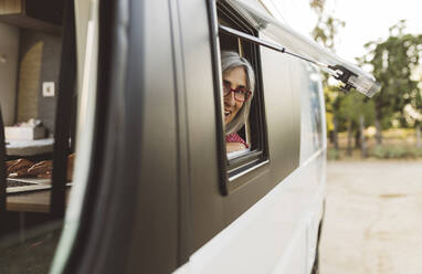 Lächelnde reife Frau schaut aus dem Fenster eines Wohnmobils - JCCMF06996