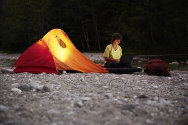 Geschäftsfrau mit Laptop an einem Zelt am Flussufer - CVF02096