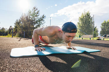 Sportsman practicing push-ups on exercise mat at park - VPIF06906