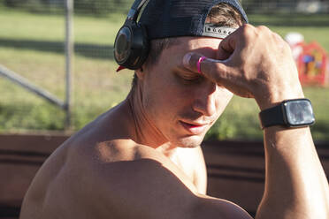 Shirtless athlete wearing smart watch listening music through wireless headphones on sunny day - VPIF06914