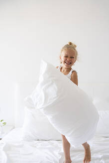 Glückliches Mädchen mit Kissen, das Spaß auf dem Bett hat - SVKF00448