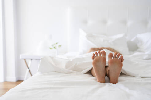 Füße eines Mädchens unter einer Decke im Bett - SVKF00450