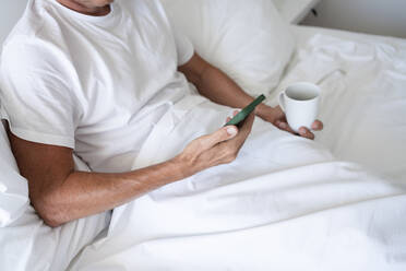 Mann mit Smartphone auf dem Bett sitzend - SVKF00470