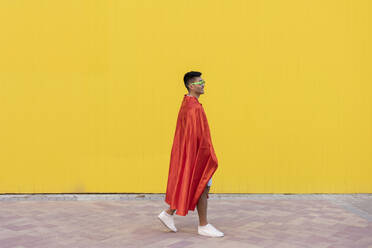 Junger Mann mit rotem Superheldenumhang geht vor gelber Wand - JCCMF07014