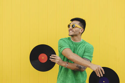 Happy young man having fun with vinyl records in front of wall - JCCMF07023