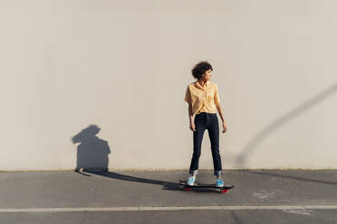 Woman skateboarding in front of wall on sunny day - MEUF07575