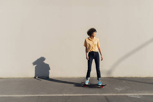 Frau auf dem Skateboard vor einer Mauer an einem sonnigen Tag - MEUF07575
