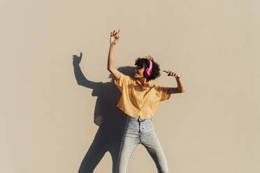 Unbekümmerte Frau tanzt mit Kopfhörern vor einer Wand - MEUF07598