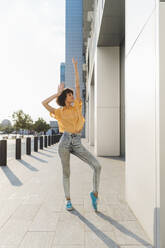 Carefree woman with hand raised dancing on sidewalk by building - MEUF07617