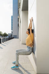 Woman with arms raised doing wall sit - MEUF07620