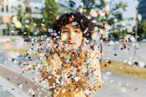 Young woman blowing confetti from hands - MEUF07622