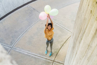 Frau mit erhobenen Armen und Luftballons auf dem Fußweg stehend - MEUF07631
