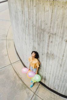 Frau mit bunten Luftballons an der Wand lehnend - MEUF07634