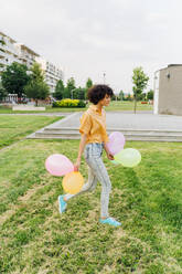 Junge Frau mit bunten Luftballons spazieren auf Gras im Park - MEUF07636