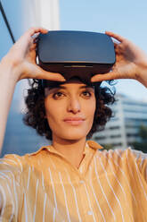 Contemplative woman holding virtual reality headset - MEUF07647