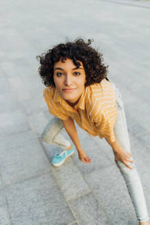 Lächelnde junge Frau mit Hand auf dem Knie auf dem Fußweg stehend - MEUF07659