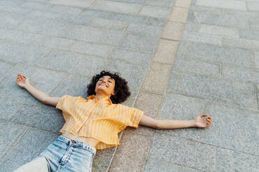 Carefree young woman with arms outstretched lying on footpath - MEUF07661