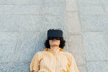 Frau liegt auf dem Gehweg und trägt ein Virtual-Reality-Headset - MEUF07665