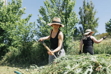 Smiling farmer wearing hat using rake at field - MRRF02317