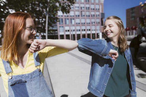 Lächelnde junge Freunde beim Ellbogenstoßen - KMKF01872