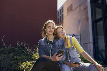 Junge Freunde mit Smartphone hören Musik über In-Ear-Kopfhörer - KMKF01881