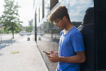 Junger Mann mit Mobiltelefon an der Wand lehnend - MEUF07672