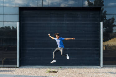 Smiling man jumping in front of building - MEUF07679