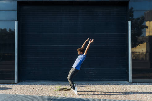 Junger Mann mit erhobenen Armen tanzt auf dem Fußweg - MEUF07680