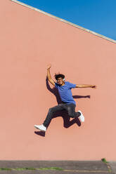 Smiling man jumping in front of wall on sunny day - MEUF07690