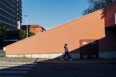 Junger Mann geht an einer Mauer in der Stadt vorbei - MEUF07706