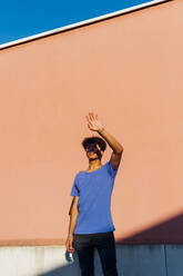 Young man shielding eyes standing in front of coral wall - MEUF07712