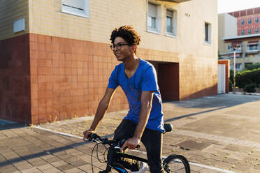 Smiling man riding bicycle in city at sunset - MEUF07736