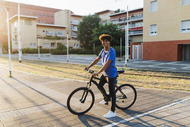 Lächelnder Mann mit Fahrrad auf einer Stadtstraße - MEUF07737
