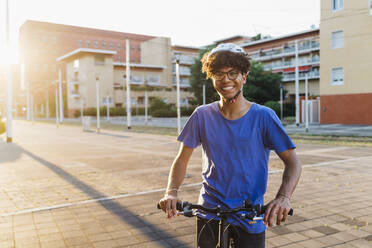 Happy man wearing helmet standing with bicycle in city - MEUF07740