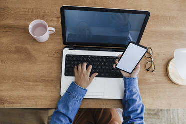 Businesswoman using laptop and smart phone at desk - EBBF05742