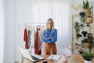 Confident fashion designer standing with arms crossed at home office - EBBF05753