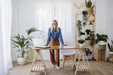 Businesswoman leaning on desk at home office - EBBF05775