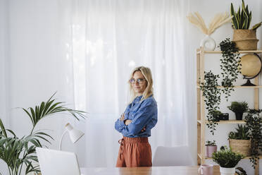 Young businesswoman standing with arms crossed at home office - EBBF05776