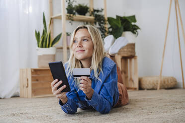 Nachdenkliche Frau beim Online-Shopping zu Hause auf dem Boden liegend - EBBF05804