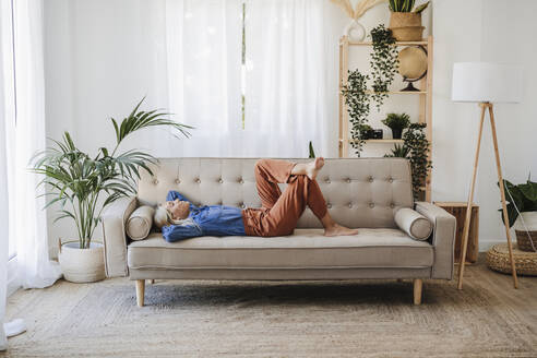 Woman relaxing on sofa in living room at home - EBBF05821