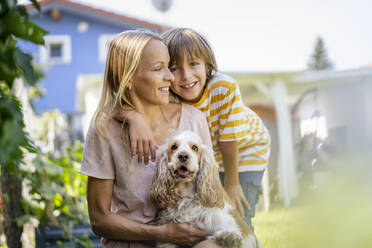 Porträt von lächelnder Mutter und Sohn mit Hund im Garten - DIGF18545