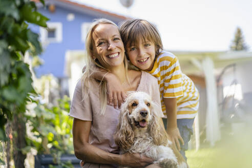 Porträt von lächelnder Mutter und Sohn mit Hund im Garten - DIGF18546