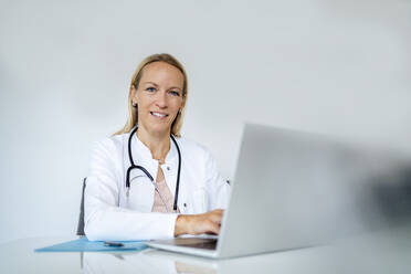 Porträt einer lächelnden Ärztin am Schreibtisch in einer Arztpraxis - DIGF18558