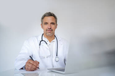 Porträt eines reifen Arztes, der in einer Arztpraxis am Schreibtisch sitzt - DIGF18566