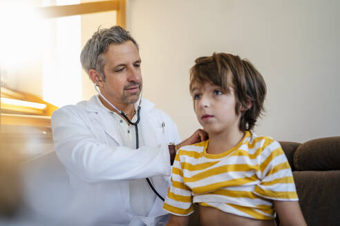 Doctor with stethoscope examining boy at home - DIGF18585