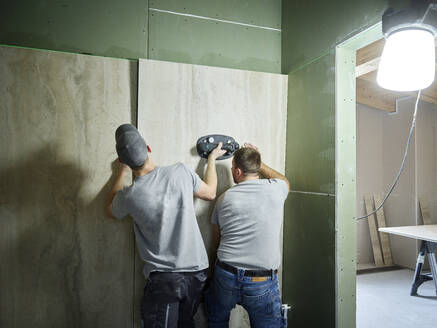 Tilers installing tiles on wall with vacuum cup at construction site - CVF02110