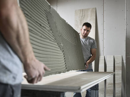 Tilers holding ceramic tile at table on construction site - CVF02113