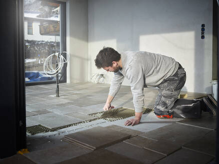 Young tiler applying adhesive on floor at construction site - CVF02115